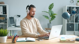 Man wearing headphones works on laptop at desk.
