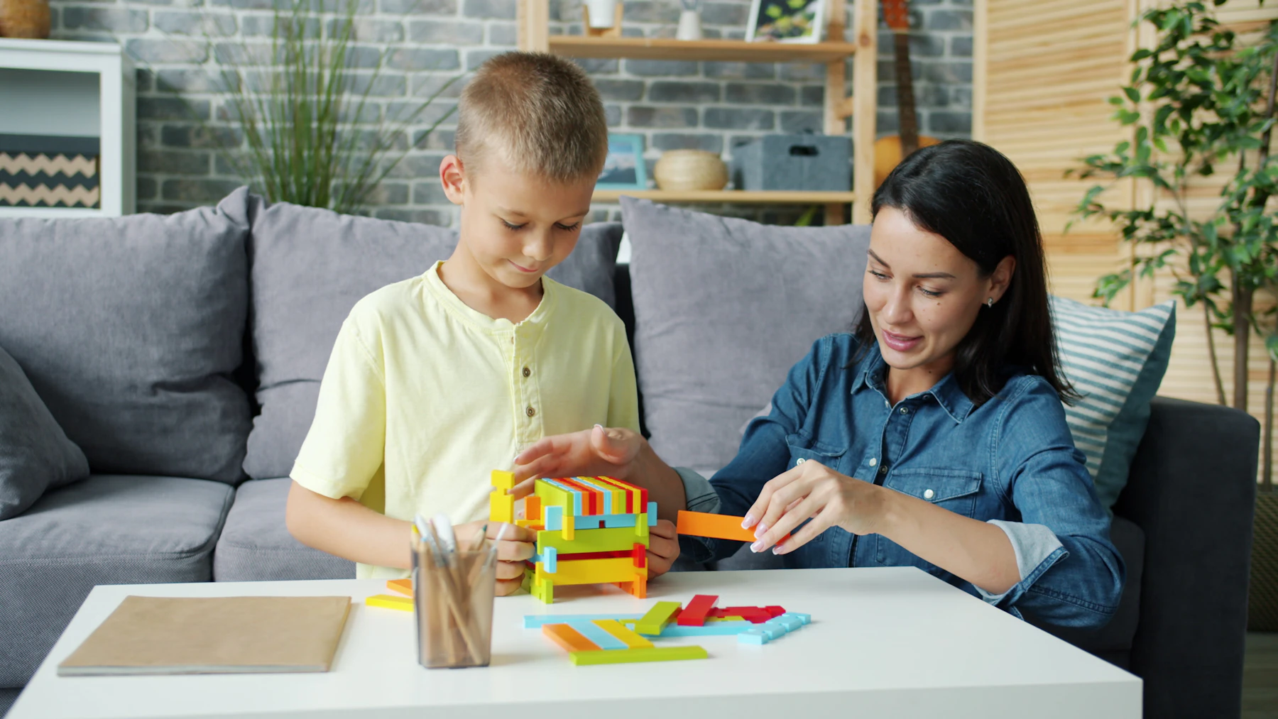 A caregiver and child building a colorful structure with educational construction pieces at a bright family table