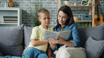 Mother and son reading a book together on sofa.