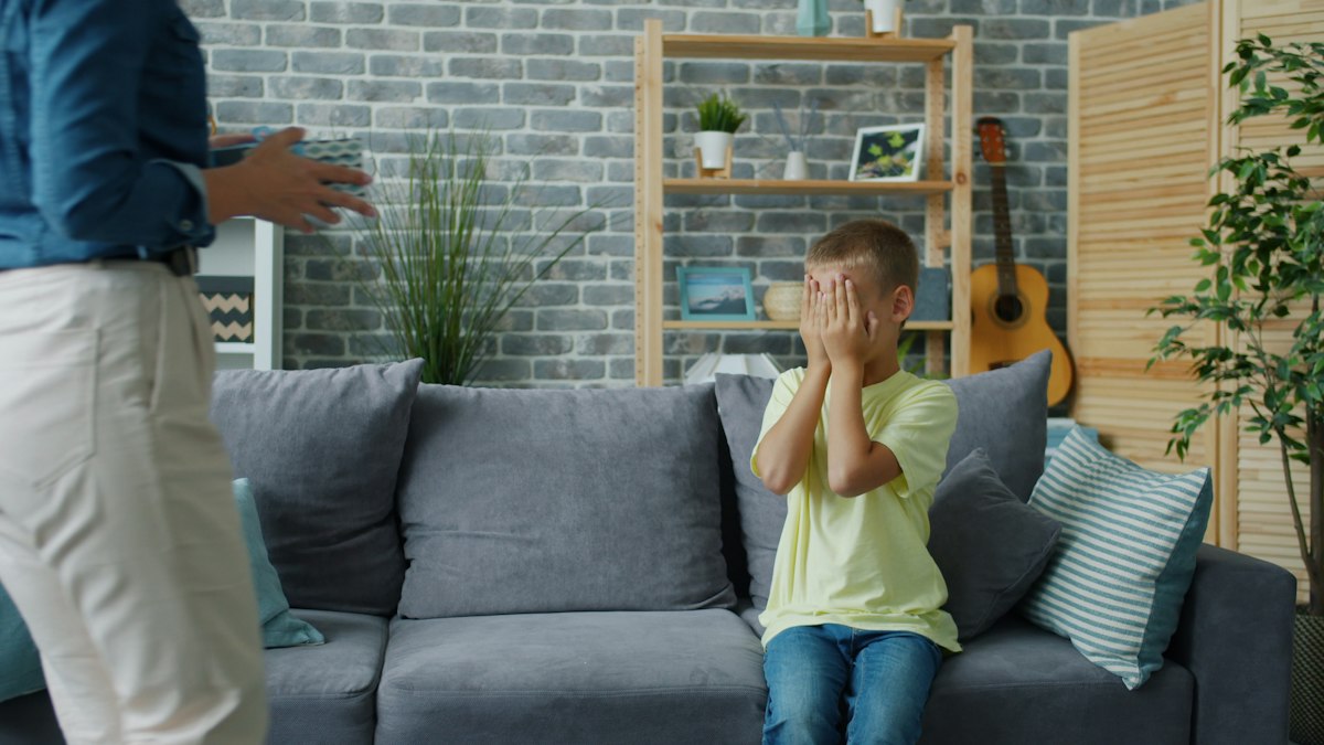 Child hiding their face while an adult stands nearby, a root of why do I cry when someone is disappointed in me