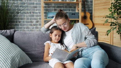 Mother and daughter reading a book together on the couch.