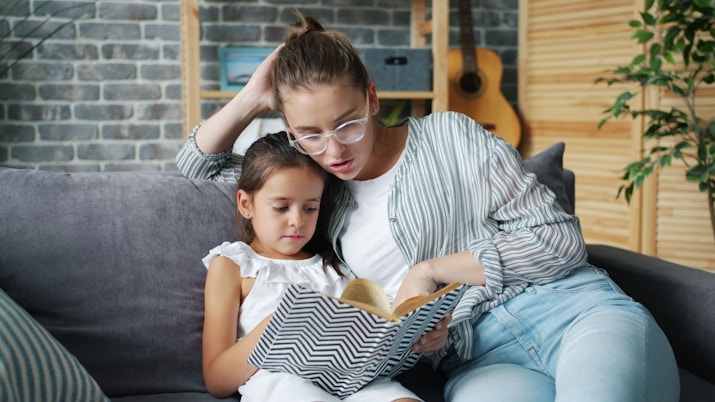 Mother and daughter reading a book together on sofa