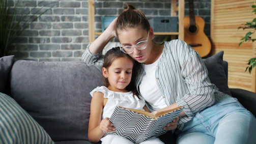 Mother and daughter reading a book together on couch