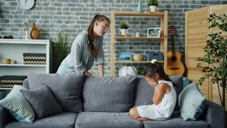 Mother scolds crying daughter on sofa in living room.