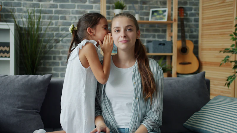 Child whispering a secret to a parent on a couch