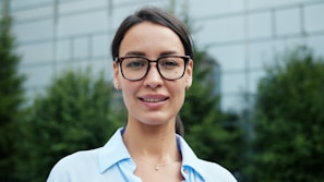 A woman with glasses smiles in front of a building.