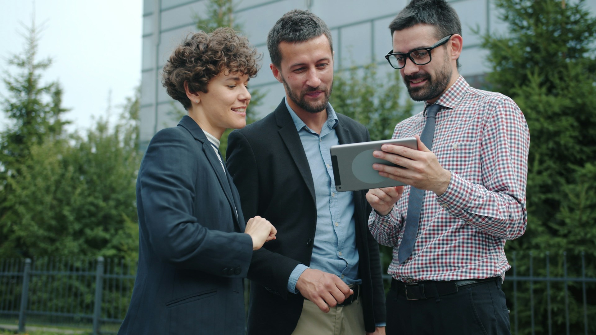 Three business people looking at a tablet outside.