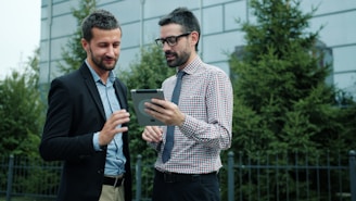 Two businessmen looking at a tablet outside office building background