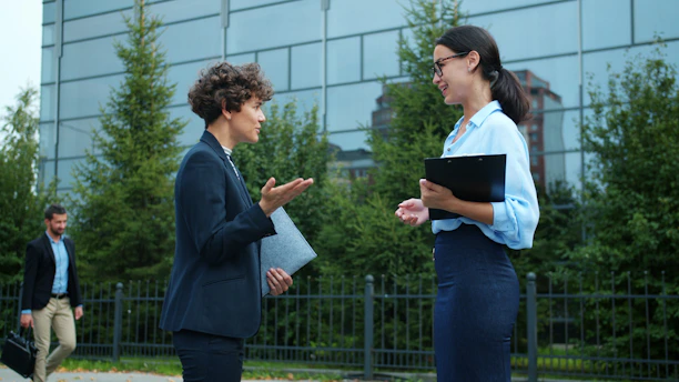 Two businesswomen talking outside modern office building.