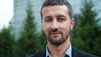 A man in a suit smiles confidently outdoors.