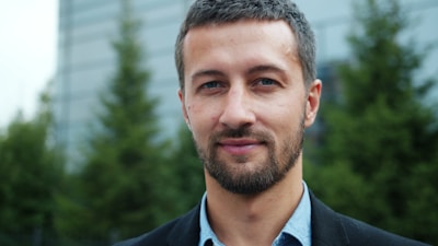 A man in a suit smiles confidently outdoors.