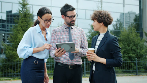 A small group of coworkers standing outside an office, looking together at a tablet screen