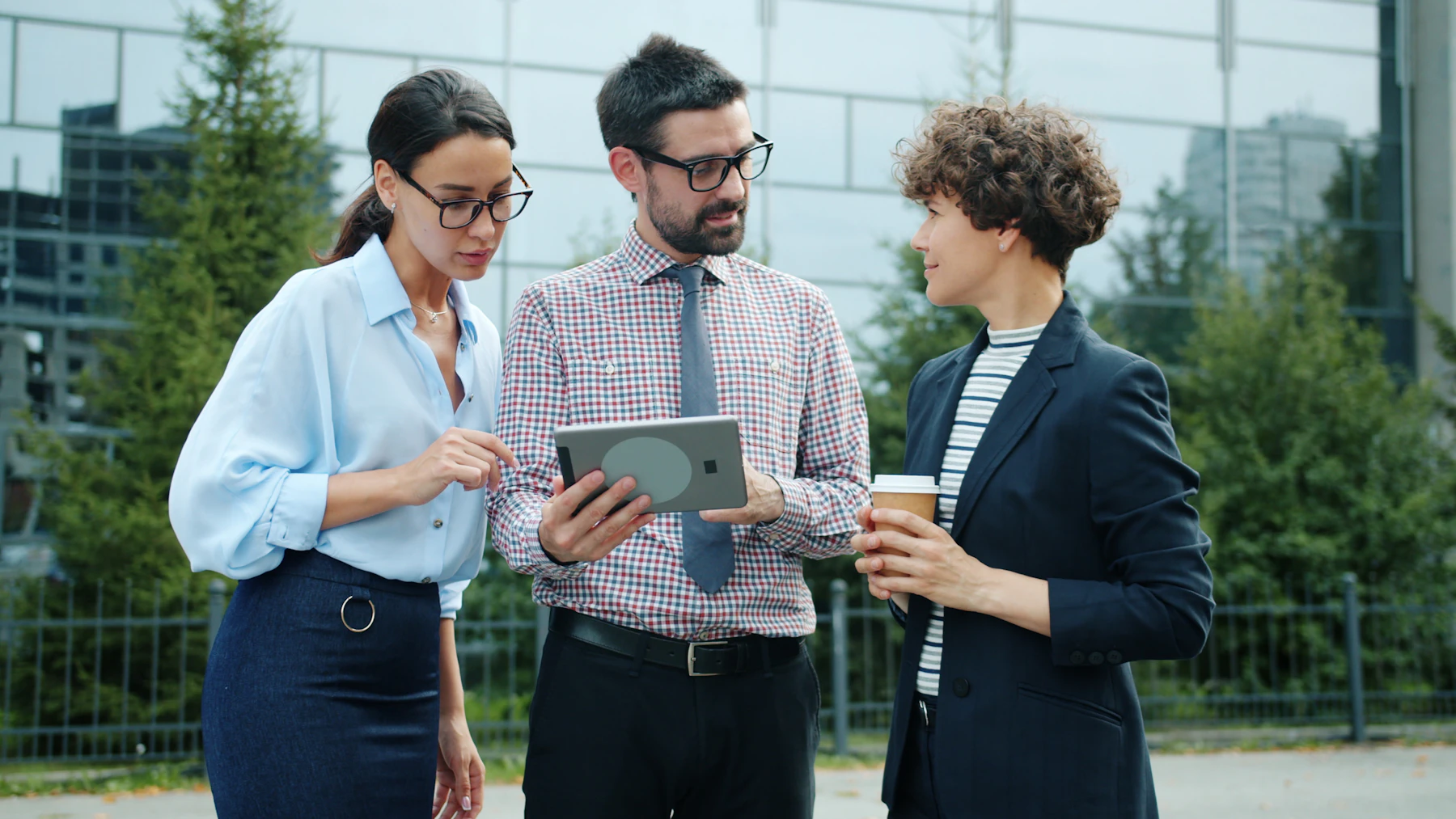 A small group of coworkers standing outside an office, looking together at a tablet screen