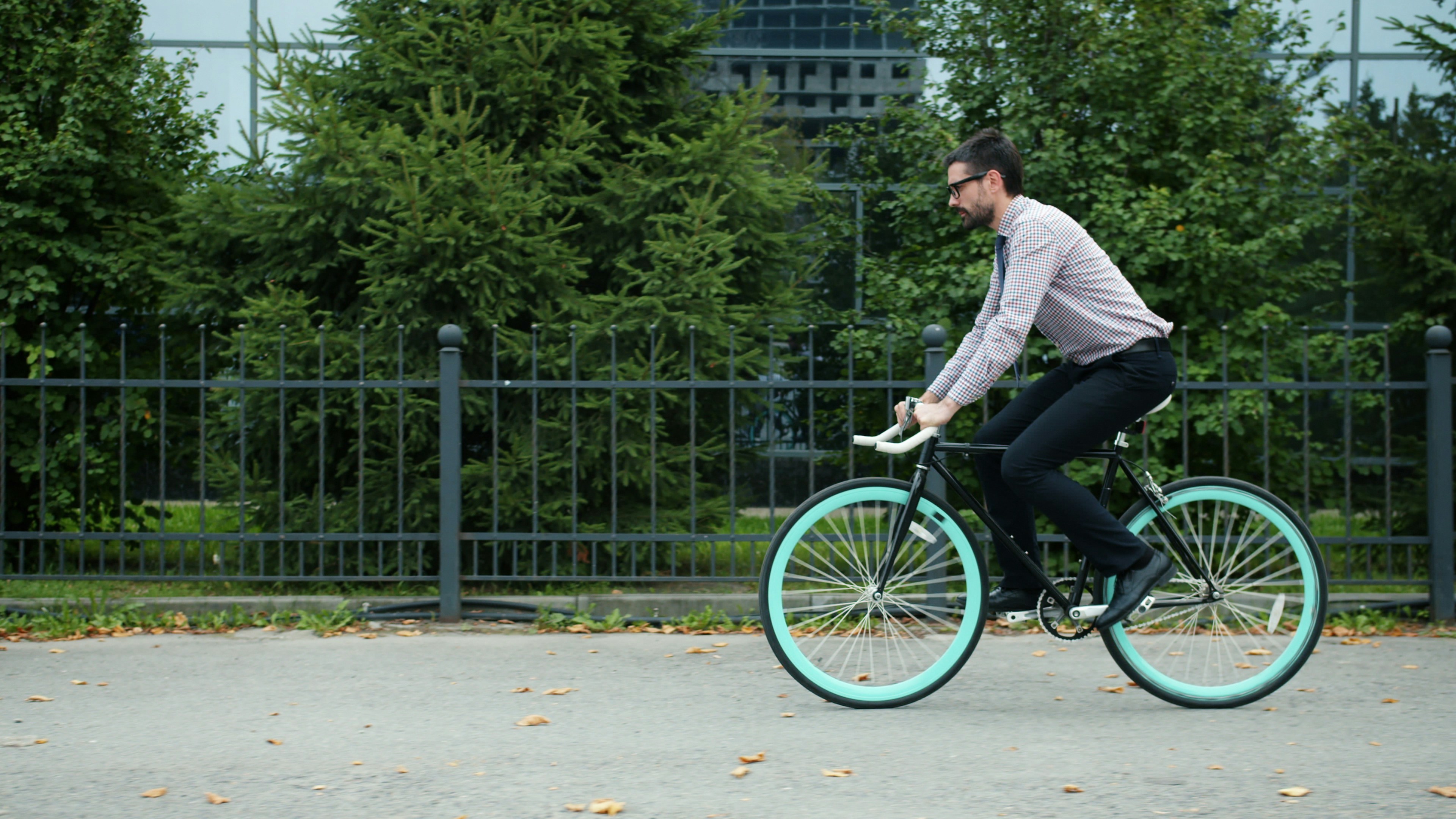 Man in glasses riding bicycle past green trees.