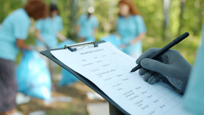 Person in gloves writing on clipboard during cleanup event.