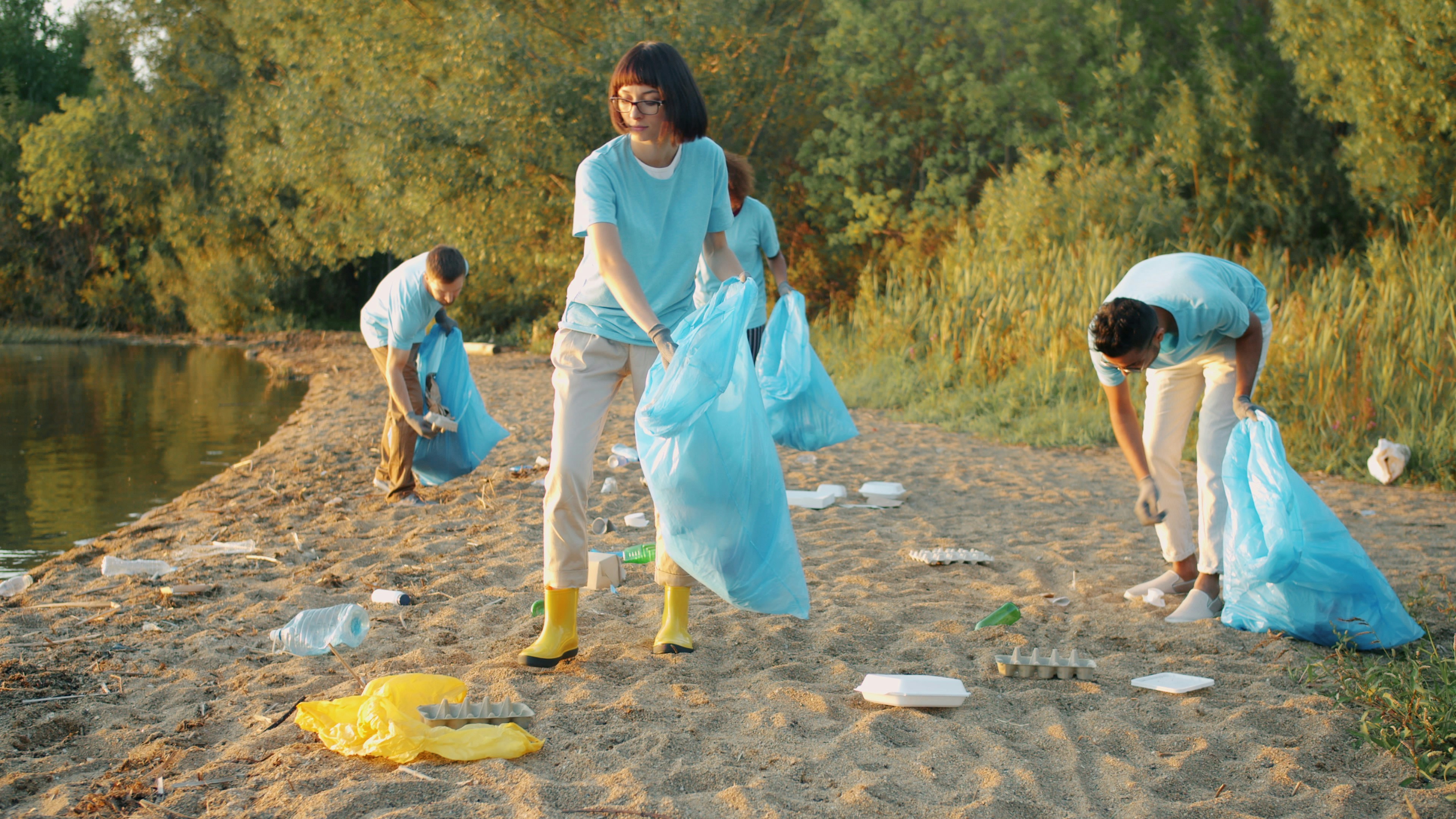 employees smiling while participating in a beach cleanup, holding bags of collected trash - team building beach