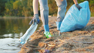 Person picking up plastic bottle near water