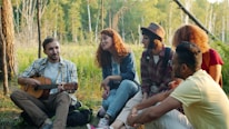 Friends enjoying music around a campfire in the woods.