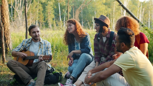 Friends enjoying music around a campfire in the woods.