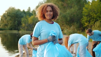 Young woman holding trash bag with volunteers cleaning beach