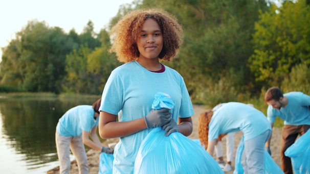 Young woman holding trash bag with volunteers cleaning beach