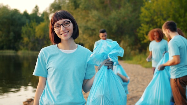 Young woman with volunteers cleaning beach with blue bags