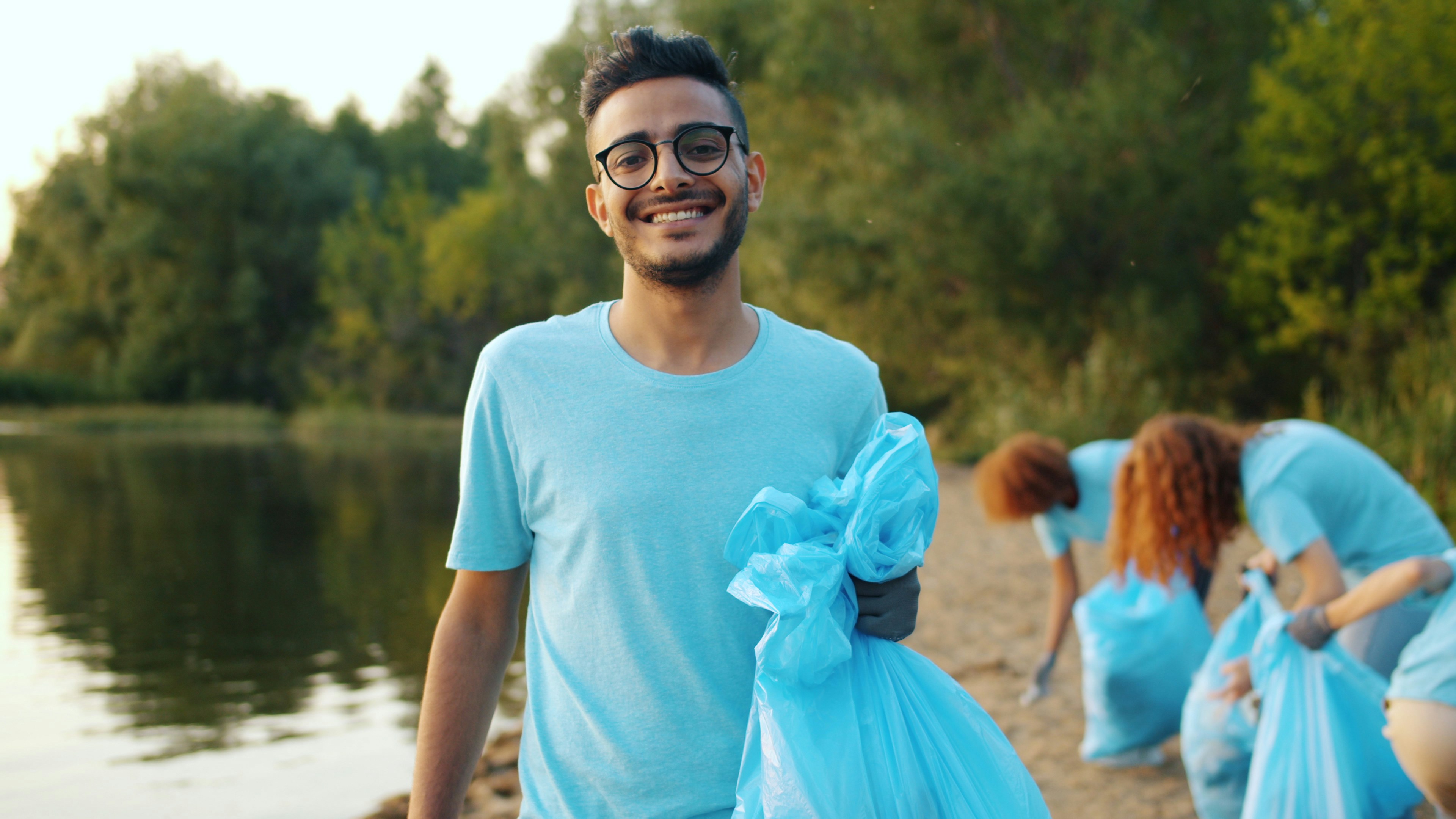 Man holding trash bag with volunteers cleaning beach