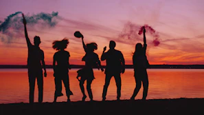 Silhouettes of friends celebrating with smoke bombs at sunset