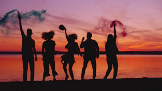Silhouettes of friends celebrating with smoke bombs at sunset