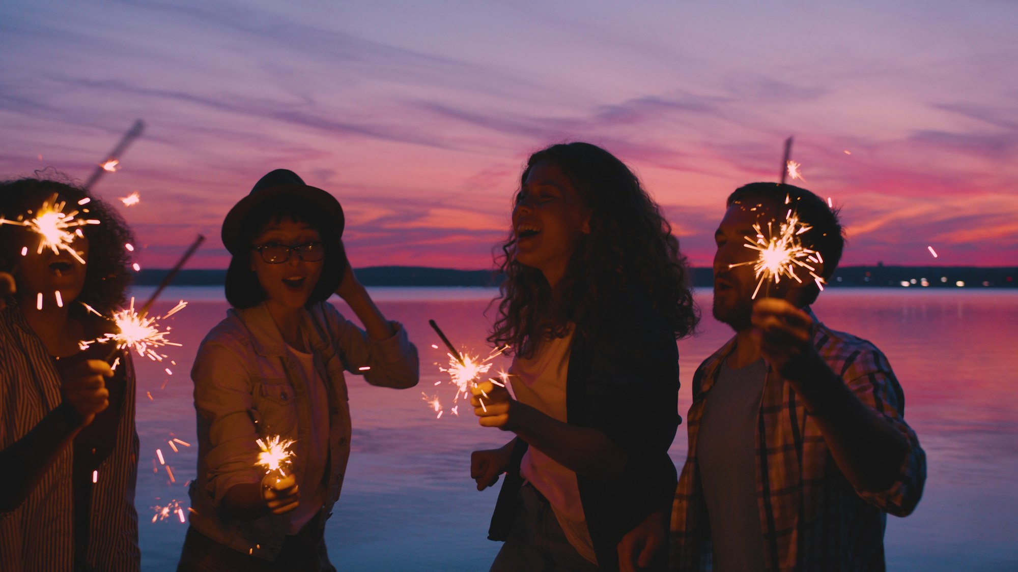 Friends celebrating with sparklers at sunset on a beach