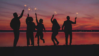 Silhouettes of people celebrating with sparklers at sunset