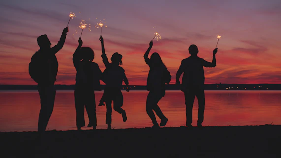 Silhouettes of people celebrating with sparklers at sunset