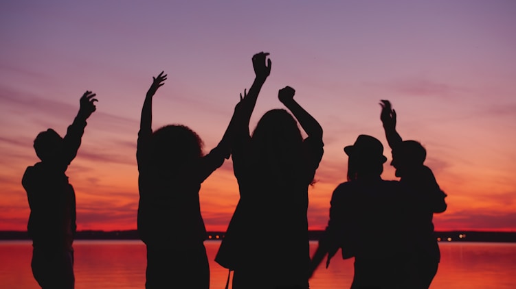 Silhouettes of people dancing against a sunset sky.