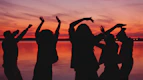 Silhouettes of people dancing at sunset by the water