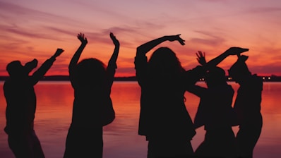 Silhouettes of people dancing at sunset by the water