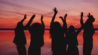 Silhouettes of people dancing at sunset by the water