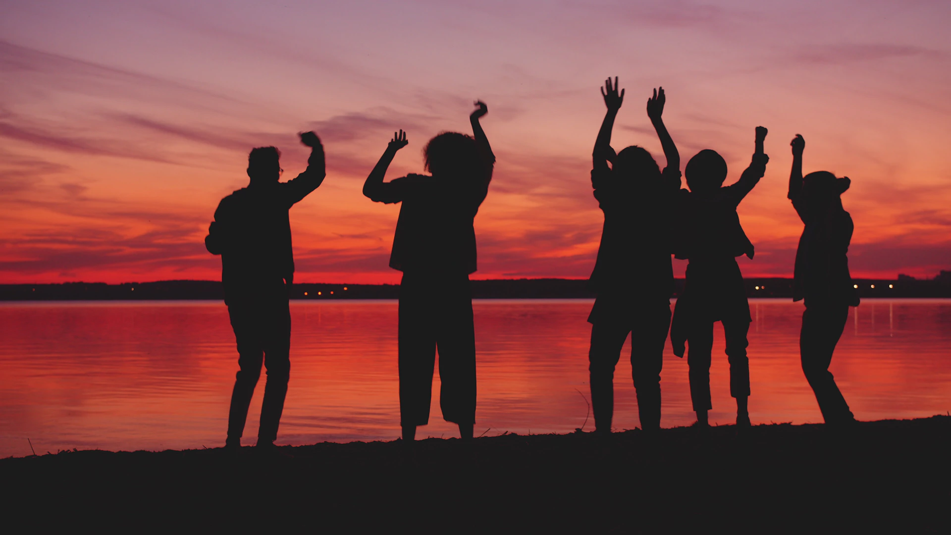 Silhouettes of people dancing by the water at sunset.