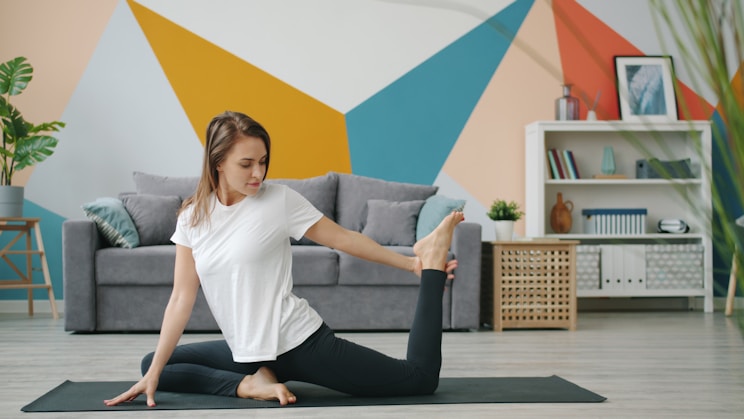 Woman practicing yoga on a mat in a living room.