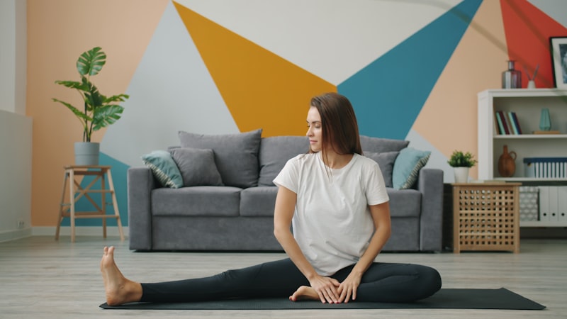 Active adult doing a seated leg stretch on a yoga mat in a living room — a gentle warm-up exercise for seniors