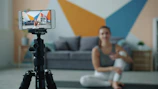 Woman recording fitness video on phone with tripod.
