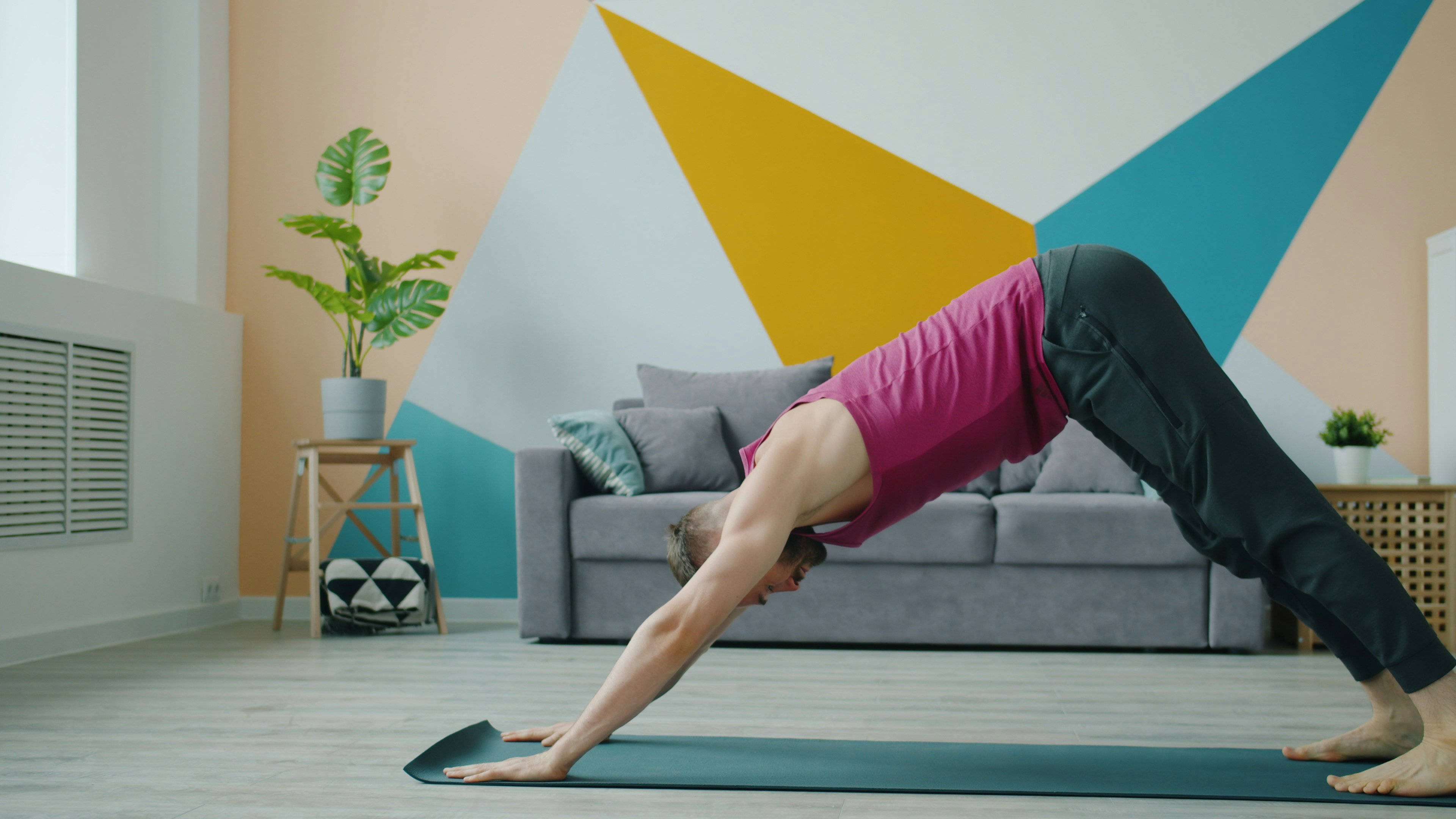 Man in downward dog pose on yoga mat indoors.