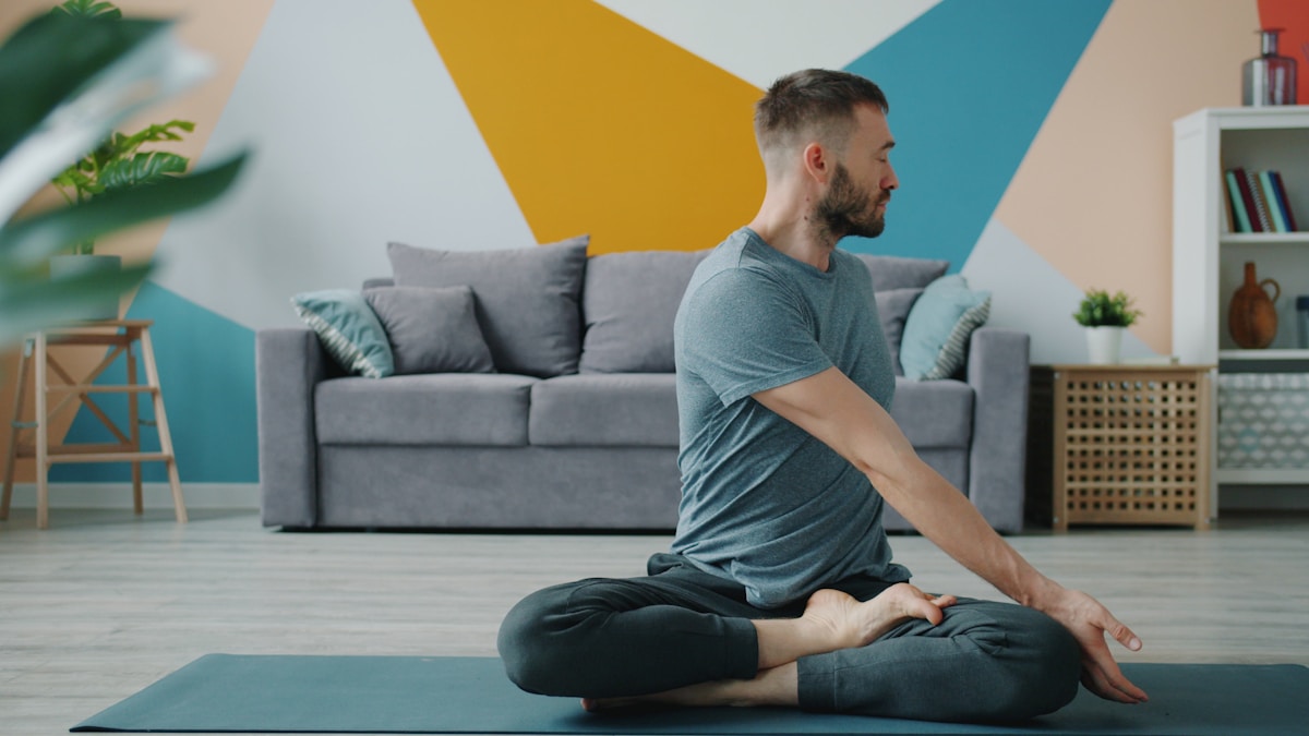 Man practicing seated mat work in a living room in front of a sofa