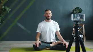 Man meditating on yoga mat recording with phone.