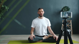 Man meditating on yoga mat recording with phone.