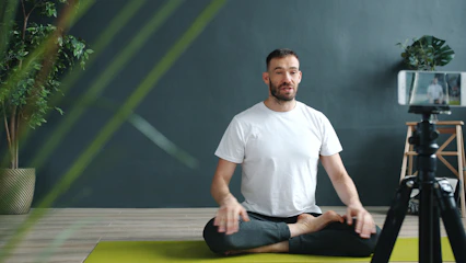 Man meditating on yoga mat recording with phone.