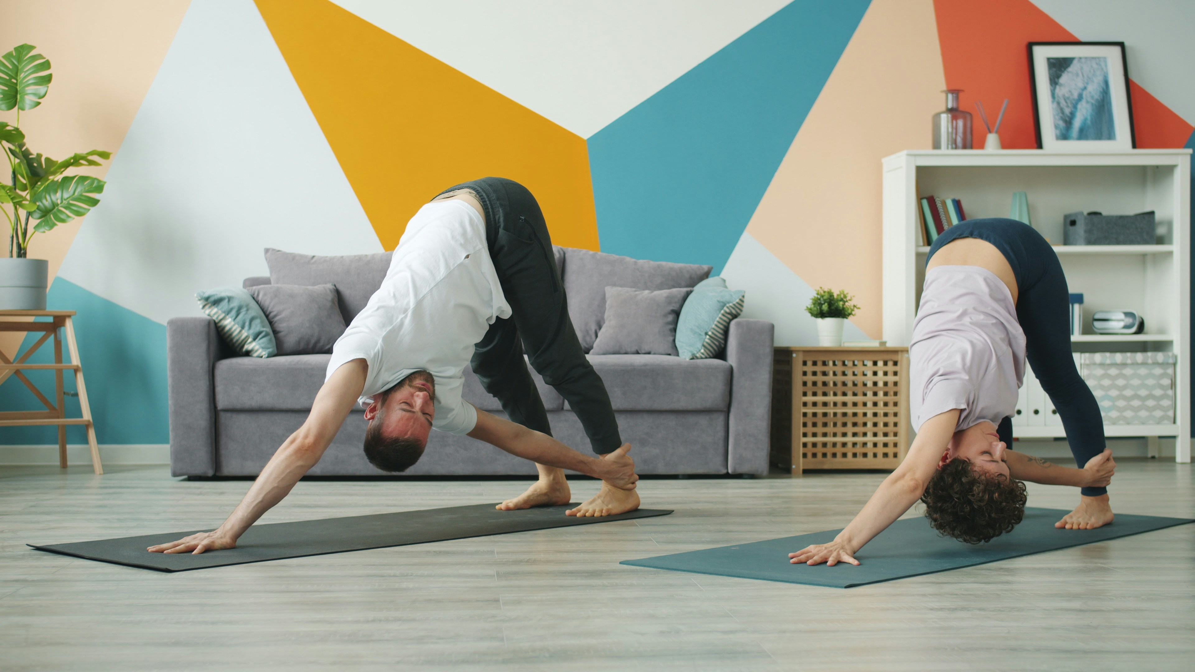 Couple practicing yoga poses in a living room.
