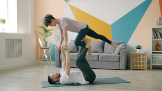 Couple doing acroyoga on a mat indoors.