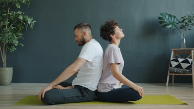 Couple meditating back to back on yoga mat.