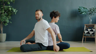 Dos personas meditando espalda con espalda sobre colchonetas de yoga.