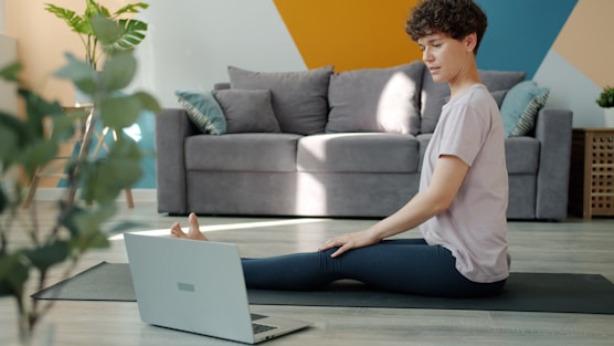 Woman stretching on yoga mat watching laptop